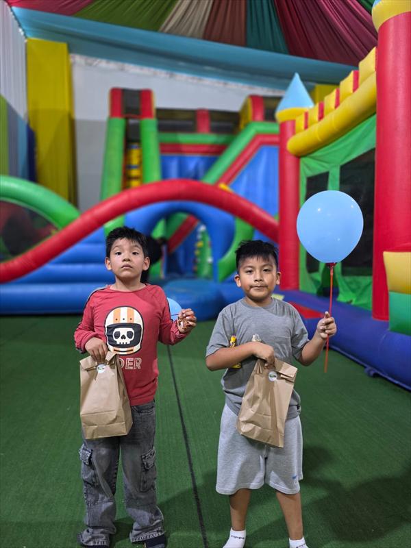 Dos niños con un globo y una bolsa de recuerdo frente a un inflable